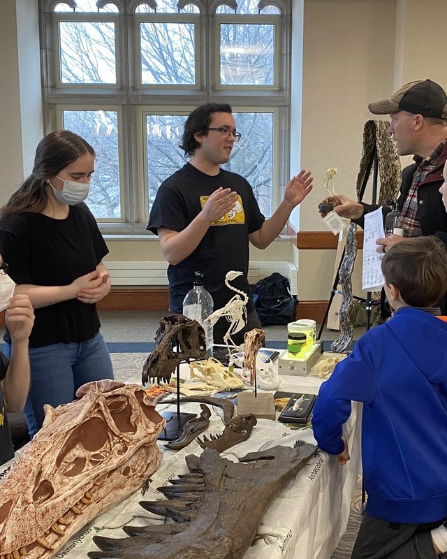 A student explaining a Deinonychus skull cast to a family at the table.
