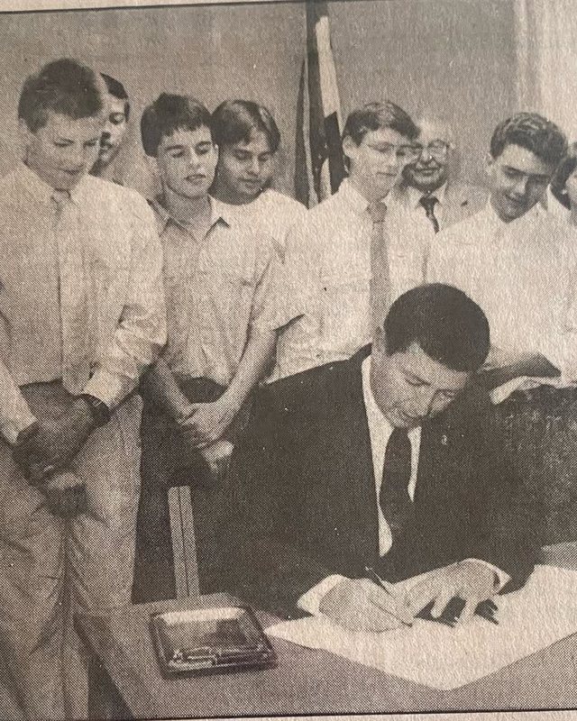 Newspaper photograph of Missouri Governor John Ashcroft signing the bill naming the crinoid the state fossil, with Pleasant Lea Junior High students looking on.