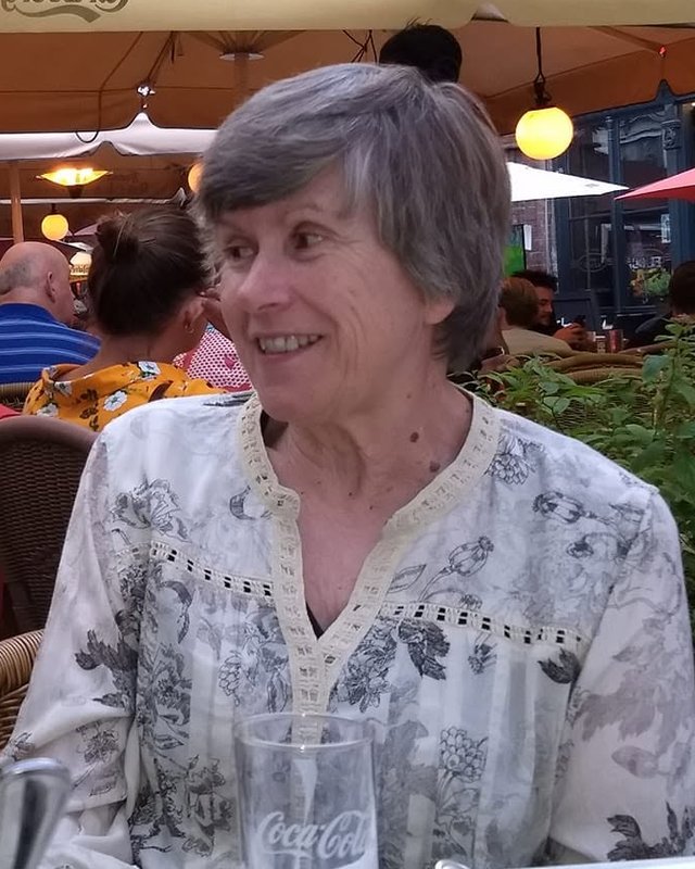 Pat Eicks smiling at an outdoor cafe table under string lights and umbrellas.
