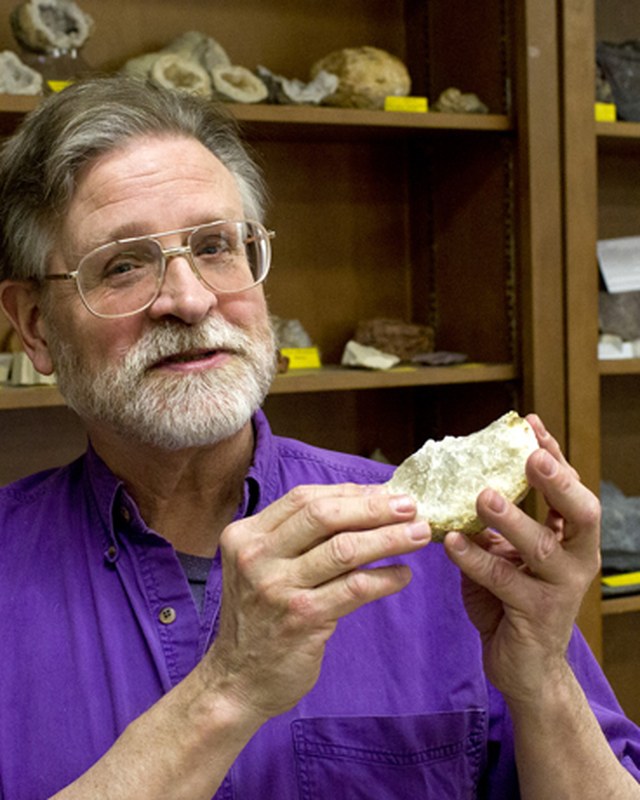 Michael Fix holding up a mineral specimen in front of shelves of labeled rocks and fossils.