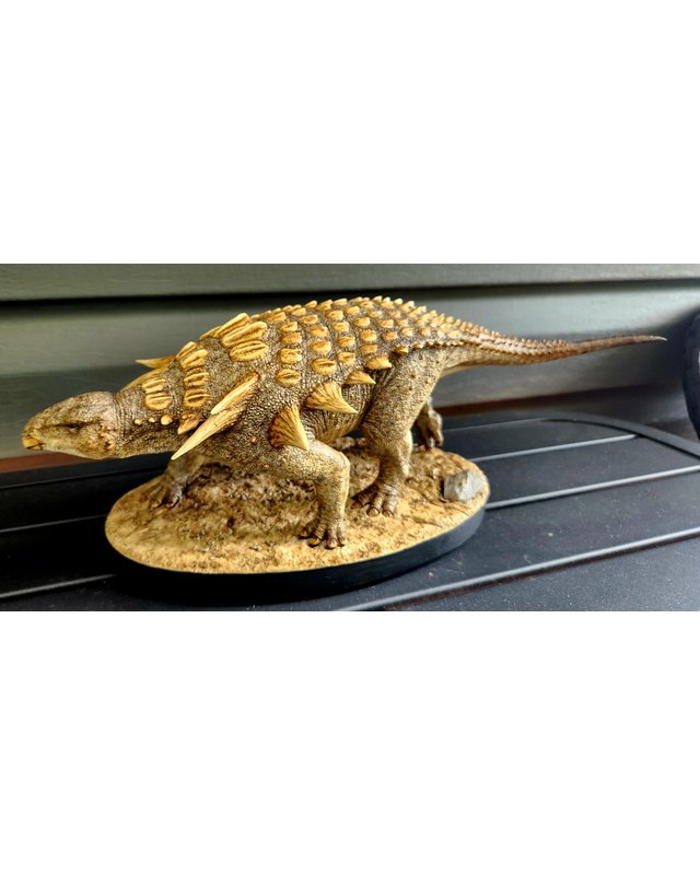 A sculpture of an armored nodosaur with pale spikes and rows of plates, walking over sandy ground, by Shane Foulkes.