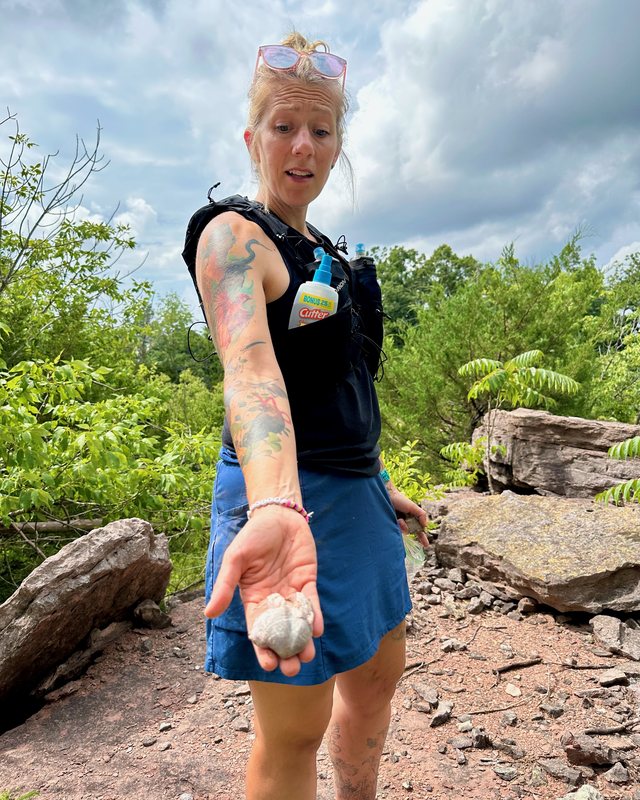 A fossil hunter holding a brachiopod in an open palm on a rocky outcrop.