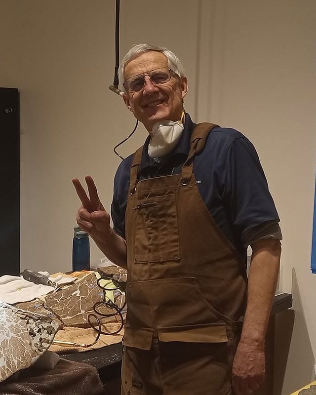 A preparator in the fossil lab beside a jacketed specimen on the bench.
