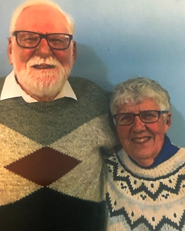 John and Dorothy Stade standing together indoors, both in hand knitted sweaters.
