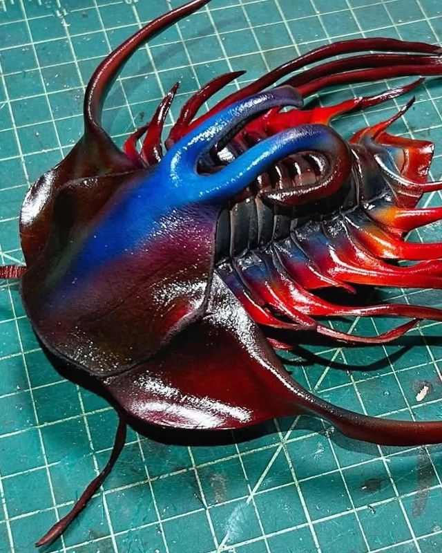 A leather arthropod sculpture in red and blue with long trailing spines, by Jason Timmermans.