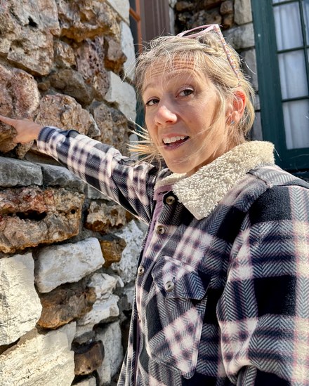 Kristen Tippit outside a stone building, reaching toward fossils in the wall.