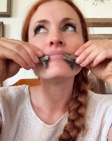Lissa Noctis holding two fossil shark teeth to her mouth like fangs.
