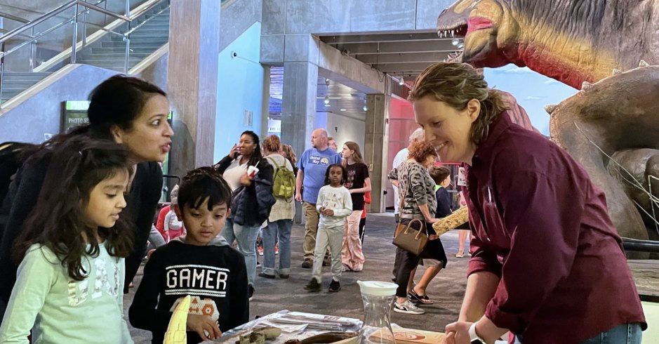 Abby Lee showing fossils to two children and their mother in the Saint Louis Science Center atrium.